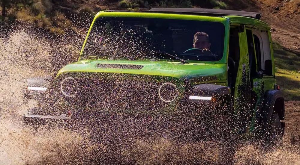 A green 2026 Jeep Wrangler driving through water.