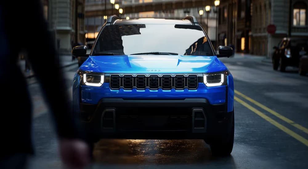 Front of a blue 2026 Jeep Cherokee driving down a road.