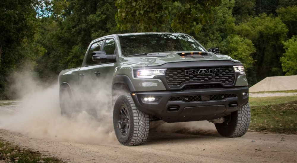 A green 2026 Ram 1500 RHO 4x4 Crew Cab driving a dirt road and kicking up dust.