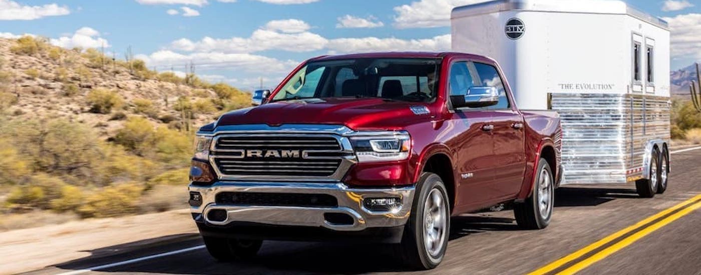 Red 2019 Ram 1500 towing a trailer on a paved road.
