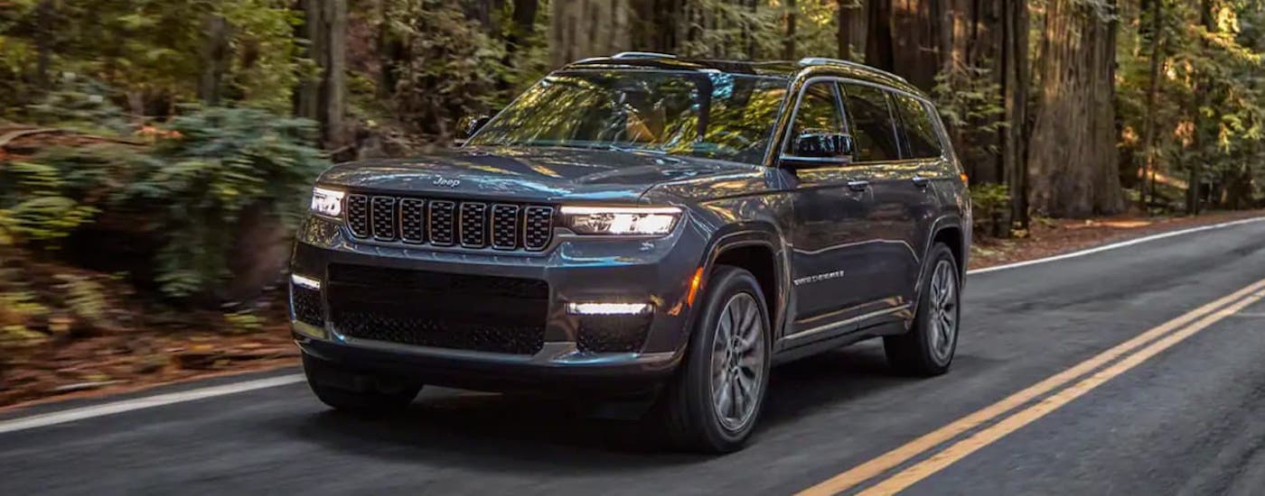 Grey 2021 Jeep Grand Cherokee L driving on a paved road in the woods.