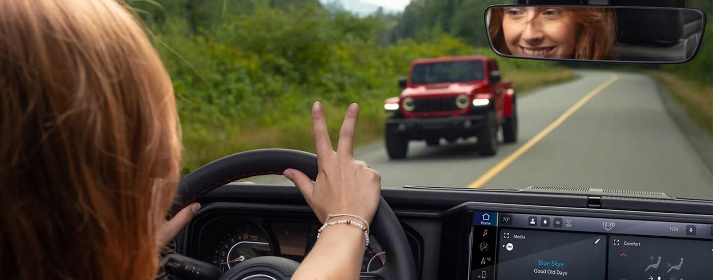 Person waving to a red 2026 Jeep Wrangler passing by