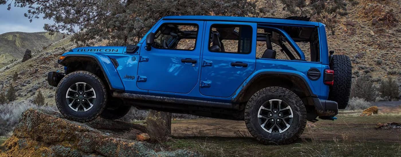 Side of a blue 2026 Jeep Wrangler off-roading on a rocky trail