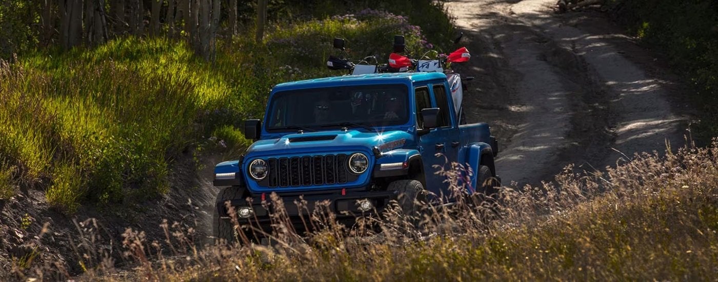 A blue 2025 Jeep Gladiator Mojave driving to a Jeep dealer.