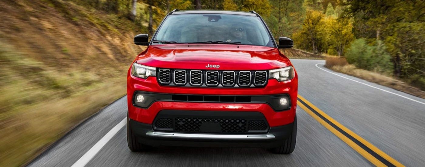 A red used 2024 Jeep Compass driving on a highway