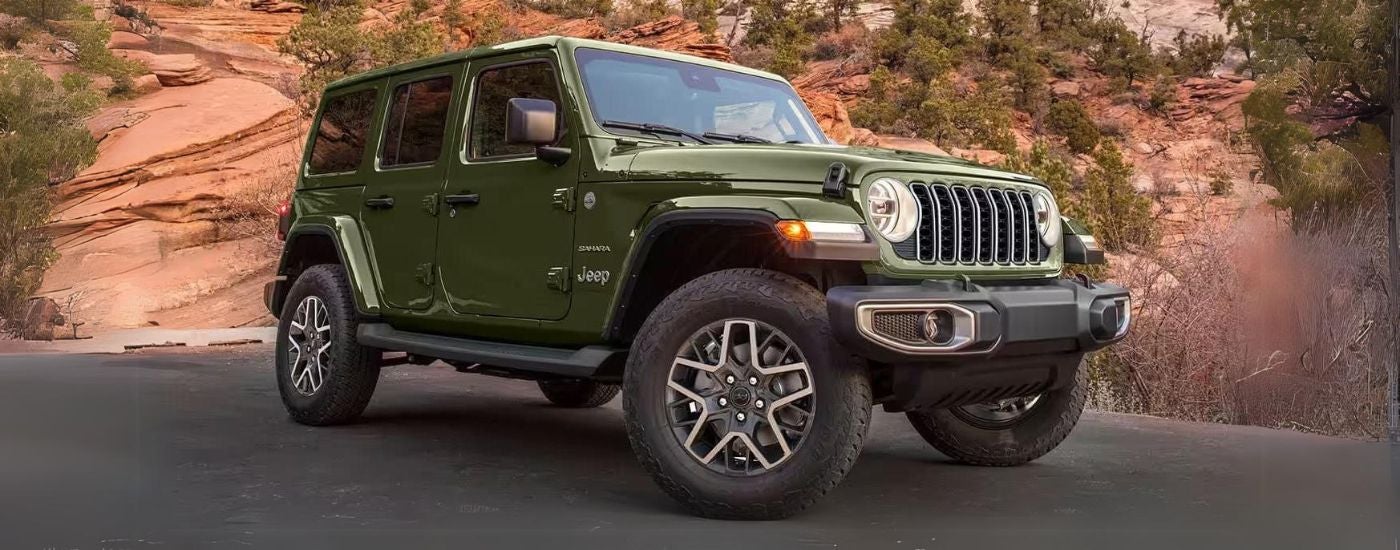 A green used 2024 Jeep Wrangler Sahara Unlimited for sale parked off-road